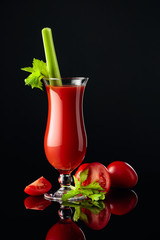 Tomato juice with celery on a black reflective background.