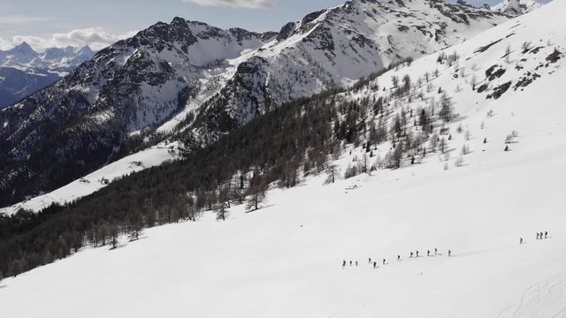 winter aerial over group of people with snowshoes hiking down a snowy slope. Winter wonderland panorama with active people.Mountains outdoor establisher.4k drone circle pan flight