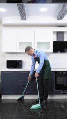 a vertical image. handsome man in tie and apron sweeping the kitchen floor