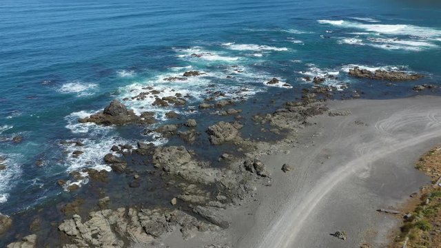 Aerial footage over rocks at black sand beach in Wellington, New Zealand