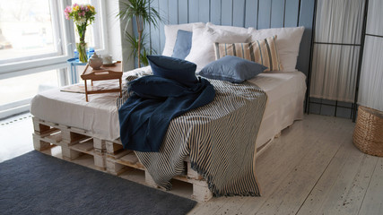 Large bed with pillows and blankets. Wooden stand for breakfast on crumpled bed in studio. Close-up of interior design room.