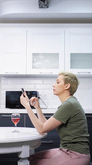  woman is resting in the kitchen with a glass of wine, e cigar uses a smartphone