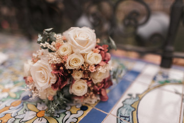 Close up photo of a beautiful wedding bouquet full of white and red roses resting in a bench of Plaza de España in Spain. Concept photography