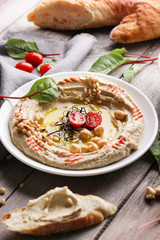 Oriental cuisine. Traditional snack hummus. It includes chickpeas, pine nuts, olive oil, spices and lemon juice. Herbs and tomatoes on a light wooden background.