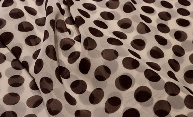 Light beige chiffon in brown peas. The material is folded randomly on a horizontal surface. Fabric sample.