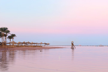 empty beach at pink sunset in Egypt. View of nice tropical empty sandy beach with umbrellas and beach beds. Calm sea view