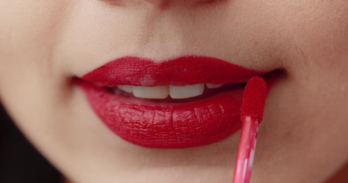 Young woman applying red lipstick with brush, extreme closeup