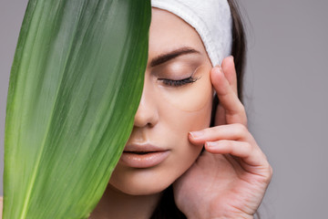 Portrait of a young beautiful woman with perfect smooth skin with a large green tropical leaf