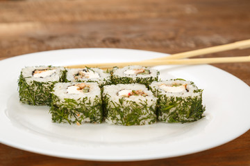 Rolls with salmon and dill on a white plate with chopsticks.