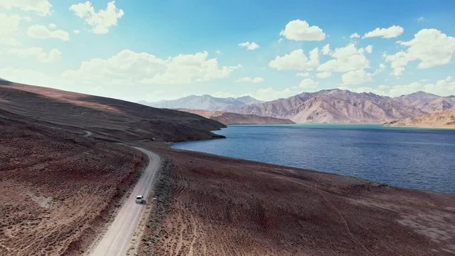 Aerial over off road 4x4 car driving along gravel trail path toward lake in arid mountains.Pamir Highway silk road travelling adventure in Tajikistan,Asia.Khorugh Bulunkul lake. 4k drone flight video