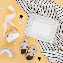 Black and white muslin swaddle blanket with photo frame and baby slippers, toys on yellow background. Set of gender neutral newborn accessories. Flat lay, top view