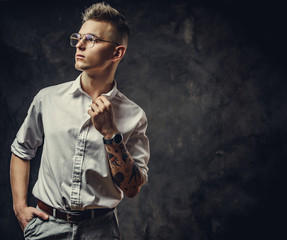 Handsome guy in a white shirt with tattoos on his hand posing in a dark studio, looking decisive and isolated on grey background