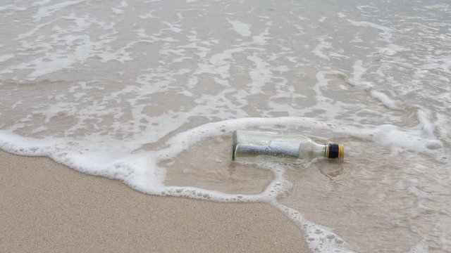 Blank message in glass bottle on beach on sand with sea waves