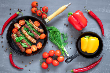 Grilled sausages in cast iron skillet or frying pan with tomatoes, dill chives and chili peppers....
