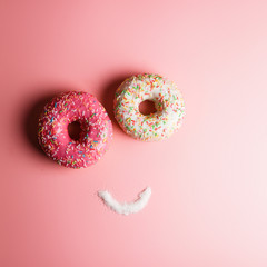 funny smiley of two donuts and sugar on a pink background with place for text, an example of junk food