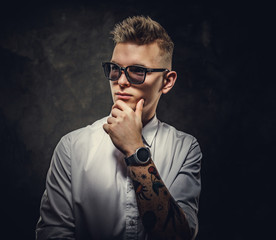Cool and tattooed hipster male model posing in a studio wearing a white shirt, sunglasses, standing...