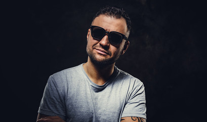 Close up portrait of a smirking adult man wearing grey t-shirt and sunglasses, looking straight into camera, looking stylish and handsome