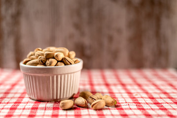Pistachios in a ceramic bowl on red checkered cloth, close-up. Space for text