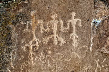 These masculine petroglyphs feature three male anthropomorph body figures each with large phallus. The are above a winding river and surrounded by bear paws.