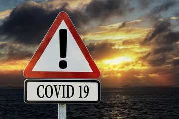 Covid-19 - Verkehrsschild vor Sonnenaufgang am Meer