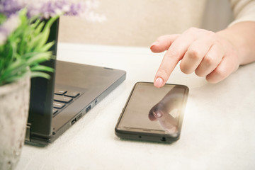 young woman hand with manicure types on black smartphone near notebook and pot plant