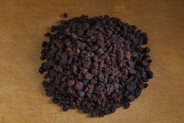 Large raisins are piled in the middle of a light wooden table.