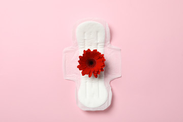 Sanitary pad with gerbera on pink background, top view