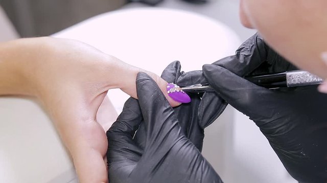 Manicurist woman in a beauty salon decorates client's nails with gel varnish with rhinestones