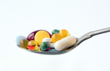 Assorted pharmaceutical medicine pills, tablets and capsules in a spoon on white background. Healthcare concept.