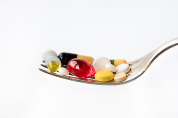 Assorted pharmaceutical medicine pills, tablets and capsules in a spoon on white background. Healthcare concept.