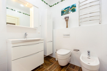 Obraz na płótnie Canvas White bathroom in a minimalist style. Bright white tiles, bathroom, toilet, sink, beige tiles on the floor. Stylish, fashionable, minimalistic