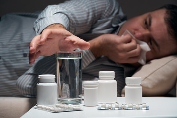 Overworked businessman is lying on the sofa and resting. Pills and glass of water near him.