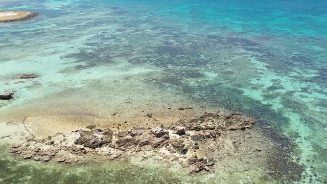 Aerial footage of drone circling a man on top of a rock formation in the middle of a beach in Noumea, New Caledonia