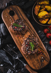 Grilled fillet steaks on wooden cutting board. Succulent thick juicy portions of grilled fillet steak served with tomatoes and roast potatoes on an old wooden board.