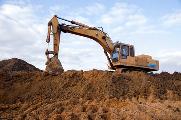 Fototapeta na wymiar Track-type excavator during earthmoving work at open-pit mining. Loader machine with bucket in sand quarry. Backhoe digging the ground for the foundation and for laying sewer pipes district heating