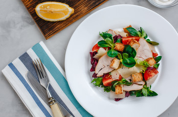 Fresh Caesar salad with delicious chicken breast, spinach, cabbage, arugula, Parmesan and cherry tomatoes on a light background. Caesar sauce, lemon, broken cheese. The concept of healthy and dietary 