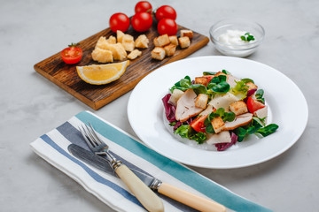 Fresh Caesar salad with delicious chicken breast, spinach, cabbage, arugula, Parmesan and cherry tomatoes on a light background. Caesar sauce, lemon, broken cheese. The concept of healthy and dietary 