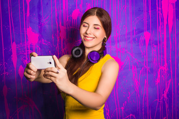 Attractive, beautiful woman with long hair and headphones on her neck, makes selfie while standing on an abstract, purple background.