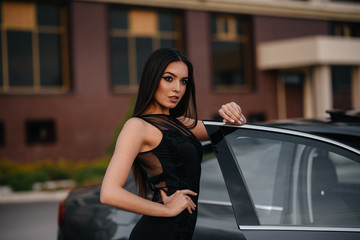 Stylish young girl stands near the car in a black dress. Business fashion and style