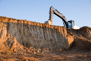 Track-type excavator during earthmoving work at open-pit mining. Loader machine with bucket in sand quarry. Backhoe digging the ground for the foundation and for laying sewer pipes district heating