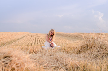 Naklejka na ściany i meble innocent beautiful girl sitting in summer harvester field alone