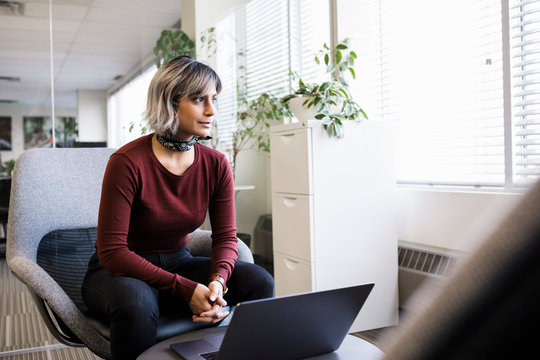 Thoughtful Businesswoman Working At Laptop, Looking Out Office Window