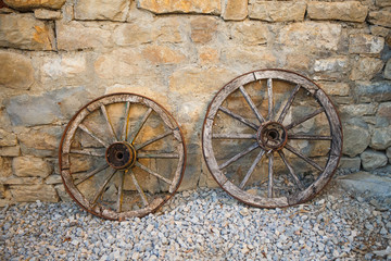 Obraz premium Old wooden cart wheels. Vintage wheels from a horse drawn cart are leaning against a stone wall