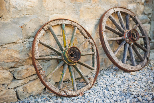 Old wooden cart wheels. Vintage wheels from a horse drawn cart are leaning against a stone wall