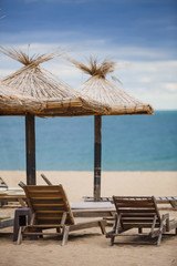 Straw beach umbrellas and wooden sun beds on a sandy beach against the sea. Beach infrastructure in Bulgaria with the inscription: 