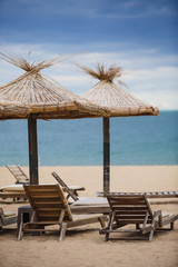 Straw beach umbrellas and wooden sun beds on a sandy beach against the sea. Beach infrastructure in Bulgaria with the inscription: 