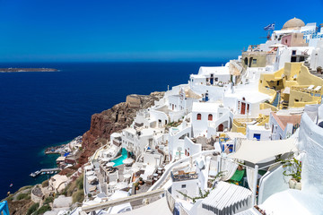 White houses of Oia town on Thira (Santorini) island with colorful volcanic cliffs and deep blue sea.