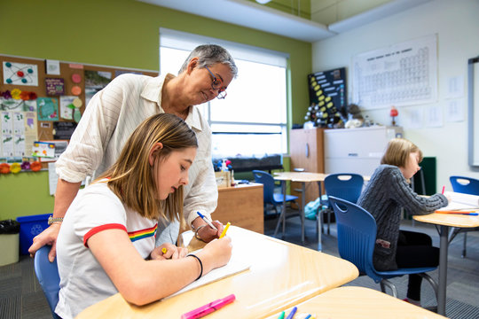 Female Junior High Teacher Helping Student With Homework In Classroom