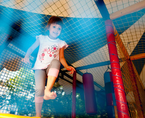 Colorful inflatables playground, girl wearing white shirt and gray pants and hanging on rings. Child looking at camera