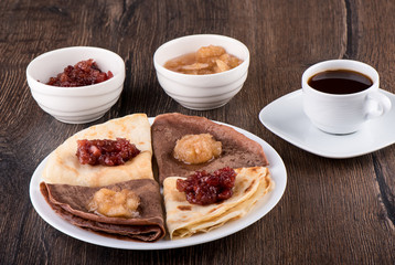 Pancakes on a white plate, apple jam of different varieties and coffee over a wooden background.